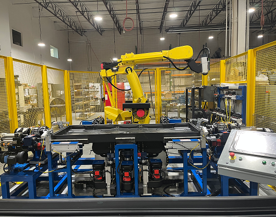 Yellow industrial robotic arm in a turn-key automation cell with safety fencing and an operator touchscreen panel.